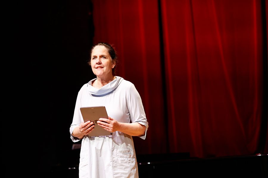 Britta Schwarz spricht zum Publikum auf der Bühne des Studiosaals vor rotem Vorhang