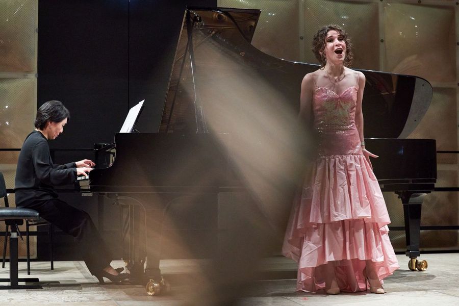 Ein Studentin in einem bunten Kleid singt auf der Bühne, neben ihr eine Studentin am Klavier