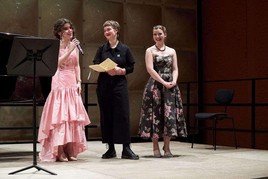 Drei Studentinnen stehen auf der Bühne, eine hält ein Mikrofon