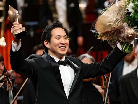 Dirigent hält Blumenstrauss und Siegertrophäe vor Publikum in die Höhe