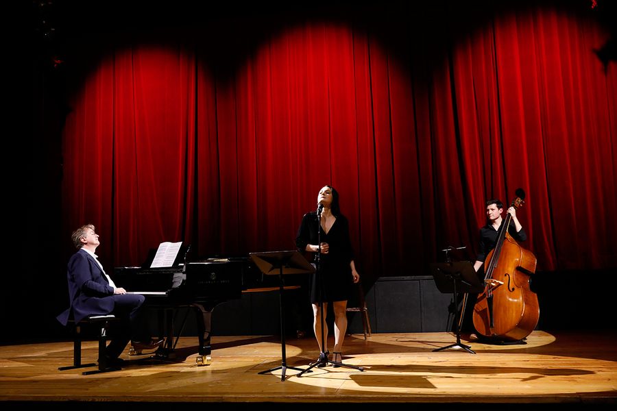 Sängerin vor Mikro, Kontrabassist und Pianist auf der Bühne des Studiosaals vor rotem Vorhang