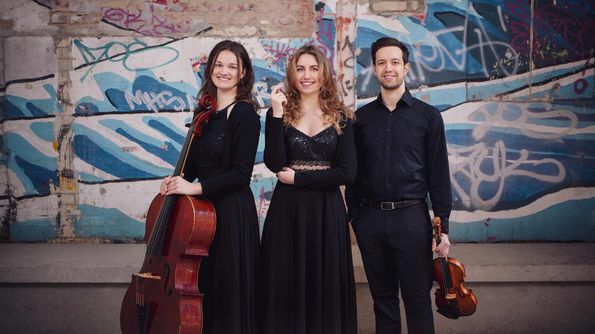 Zwei Musikerinnen und ein Musiker mit Instrumenten vor einer Graffiti-Wand