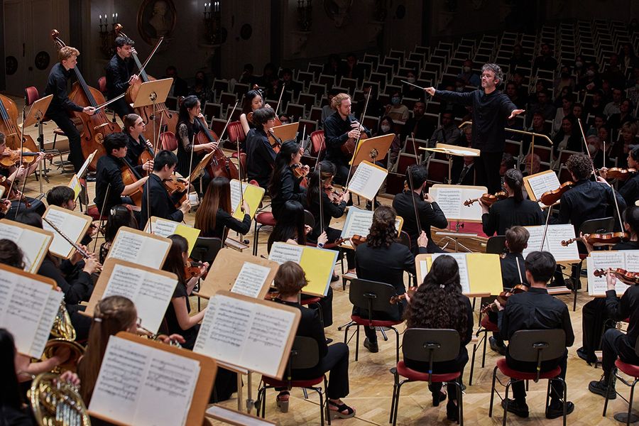Dirigent steht vor einem Orchester mit erhobenem Taktstock