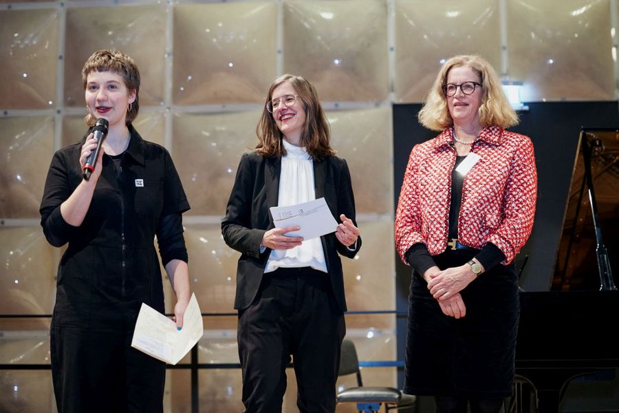 Drei Frauen stehen auf der Bühne, eine hält ein Mikrofon in der Hand