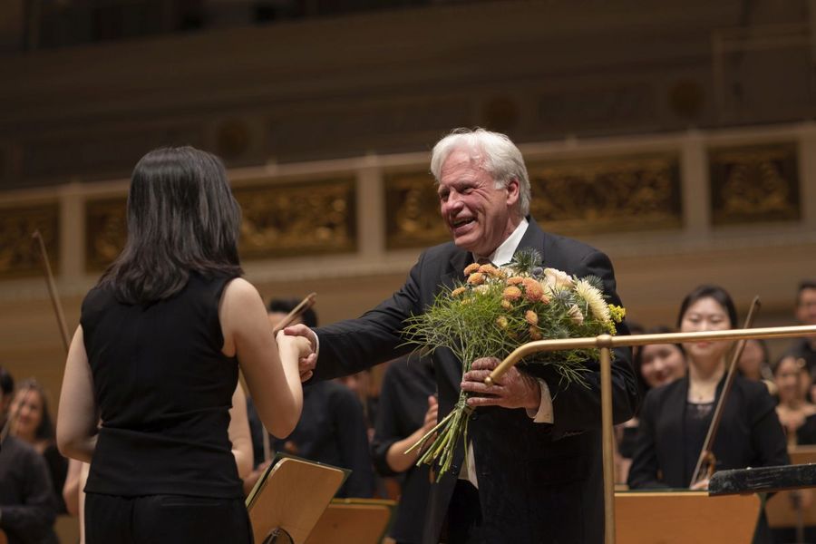 Dirigent hält Blumen in der Hand und reicht einer Frau die Hand