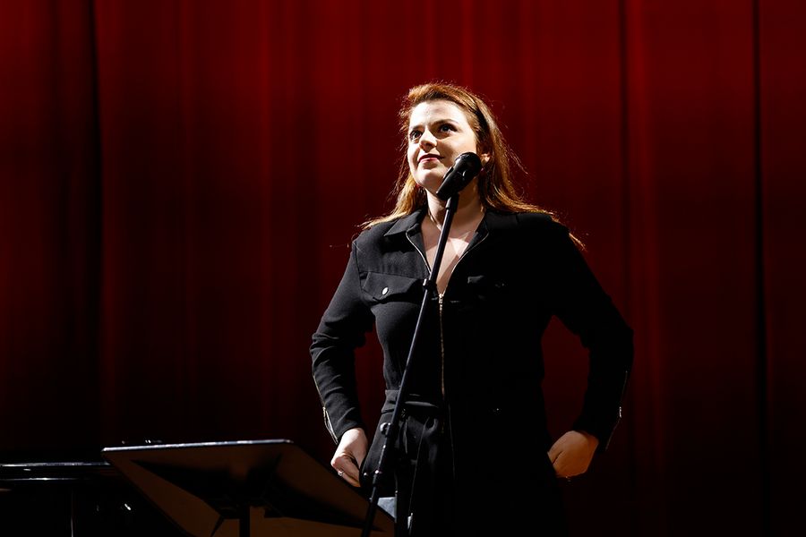 Gesangstudentin steht singend vor einem Mikro auf der Bühne des Studiosaals vor rotem Vorhang