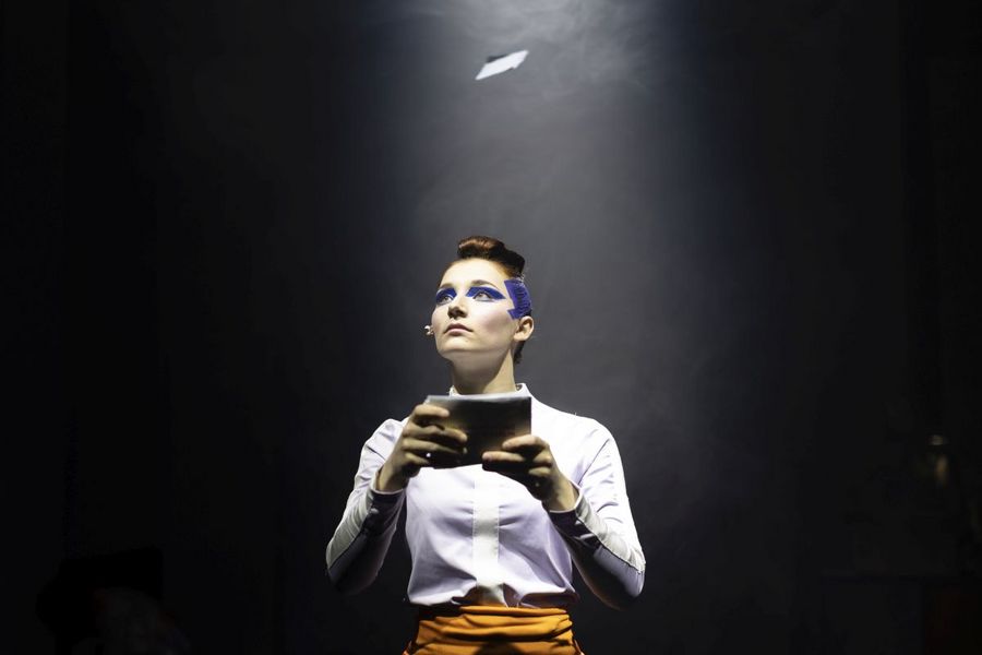 Eine Frau mit blauer Farbe im Gesicht hält Karteikarten und schaut nach oben