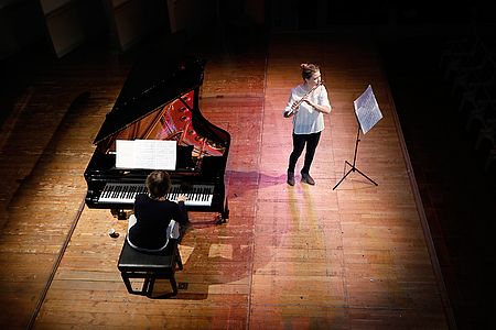 Studentin mit Querflöte und Pianistin am Flügel auf einer Bühne