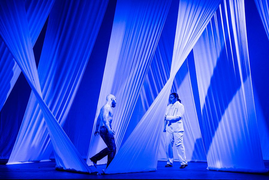 Zwei Gesangsstudierende auf einer blau beleuchteten Bühne mit weißen von der Decke hängenden Tuchbahnen