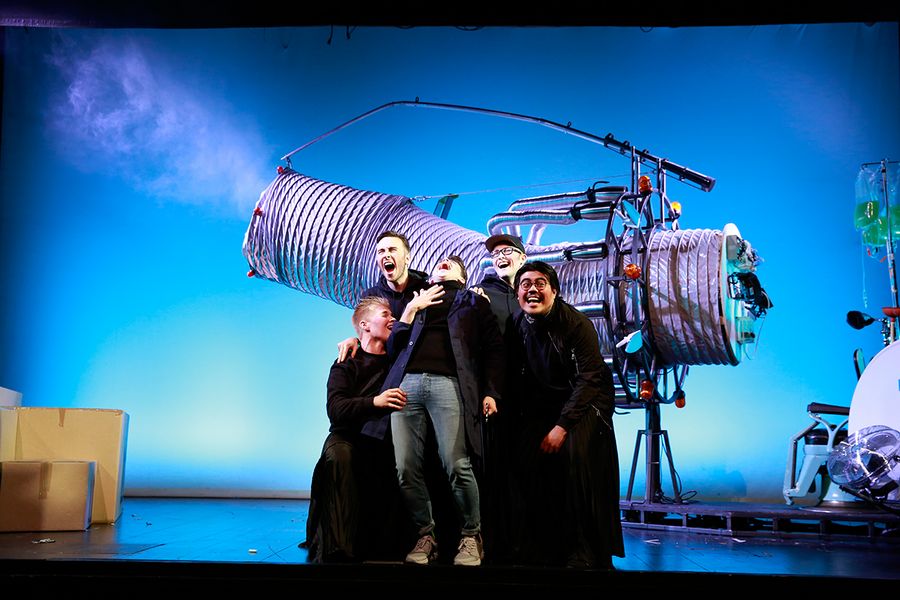 Singende Studenten auf einer Opernbühne vor einem großen Teleskop