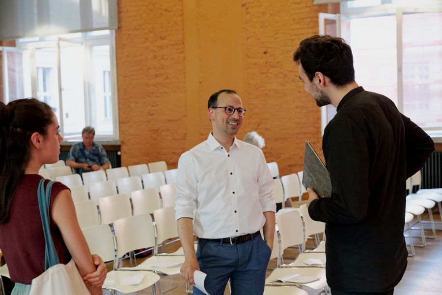 drei Menschen unterhalten sich im Hintergrund weiße Stühle