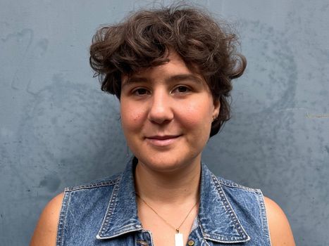 Frau mit kurzen Locken und Jeansweste vor grauem Hintergrund