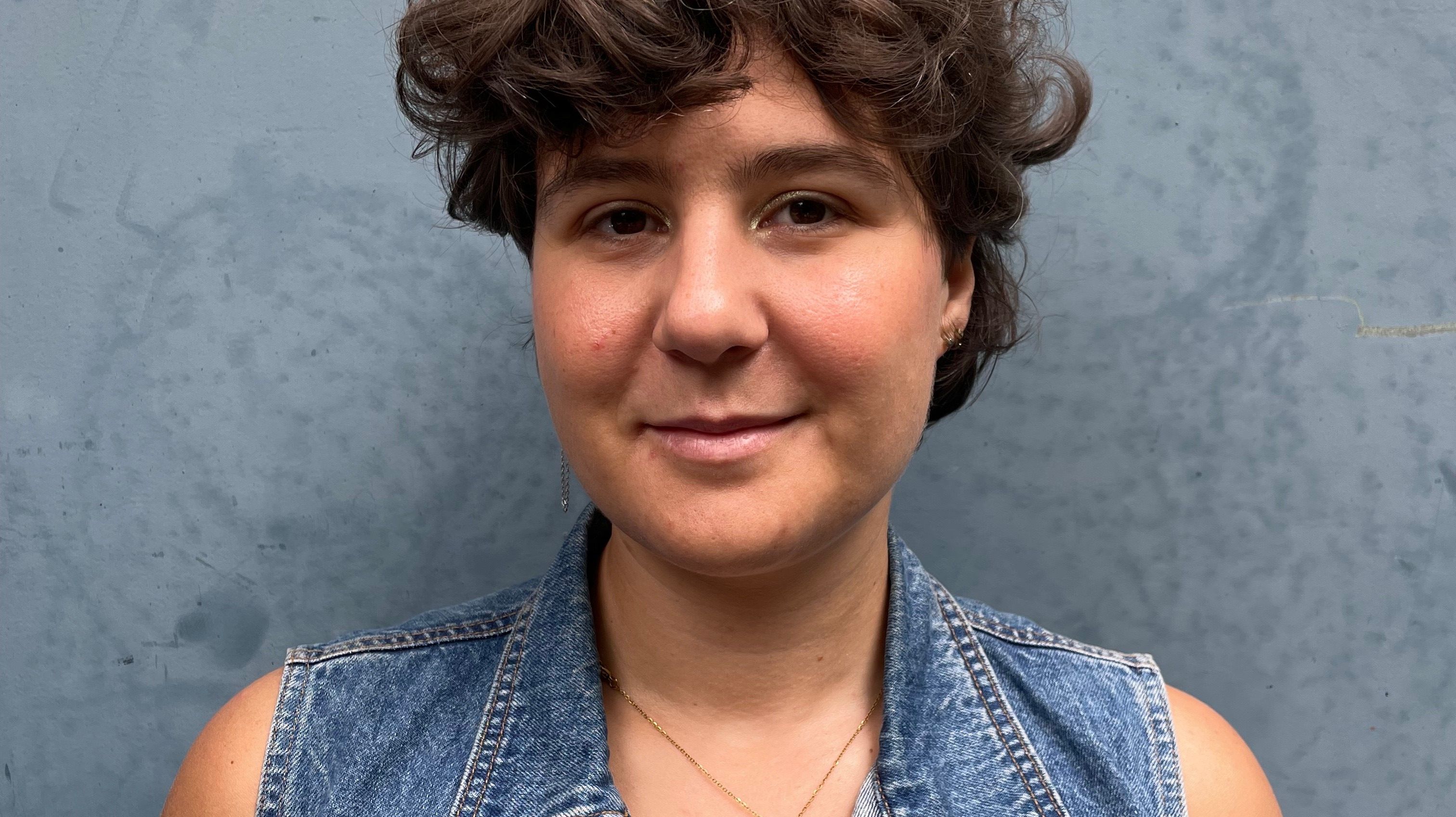 Frau mit kurzen Locken und Jeansweste vor grauem Hintergrund