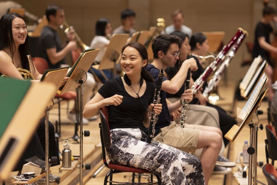 Studentin mit Klarinette sitzt im Orchester zwischen anderen Bläser*innen