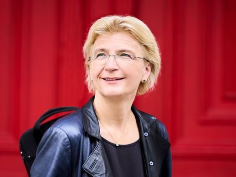 Frau mit schwarzer Lederjacke und Geigenkasten vor rotem Hintergrund 