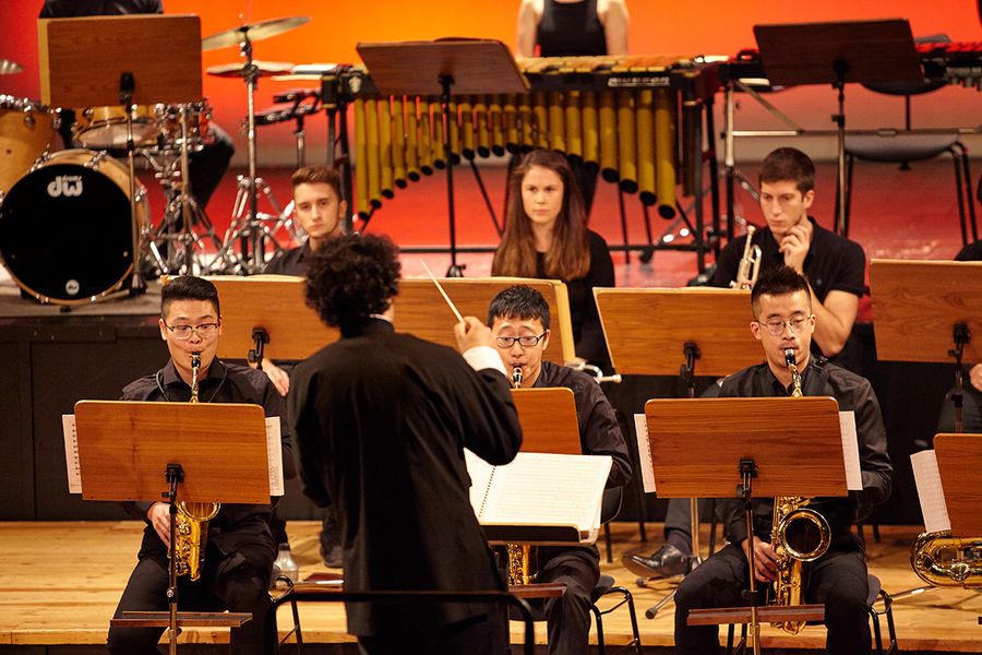 Mann dirigiert drei Studenten mit Saxophonen und drei Studierende mit Trompeten