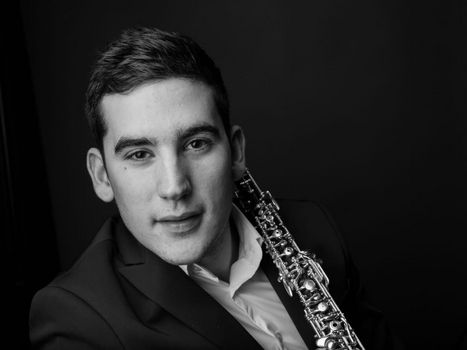 Junger Mann mit Oboe vor schwarzem Hintergrund