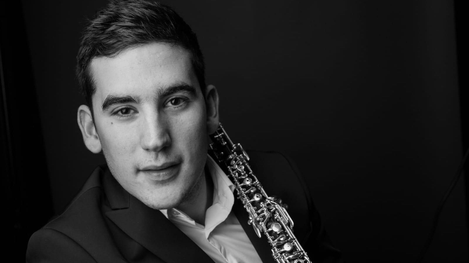 Junger Mann mit Oboe vor schwarzem Hintergrund
