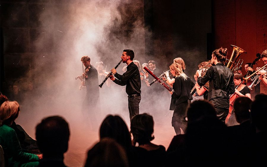 Personen mit Instrumenten stehen im Nebel auf einer Bühne