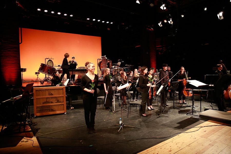 Ensemble und Solistin stehen mit Rosen in den Händen auf einer Bühne