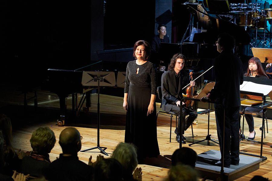 Professorin Anna Konrondi auf einer Bühne mit Orchestermusikern und Dirigent