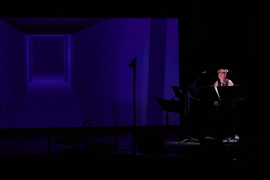 Ein Musikerin steht auf der Bühne im Studiosaal und spielt Fagott, neben ihr eine Leinwand mit einem blauen Bild