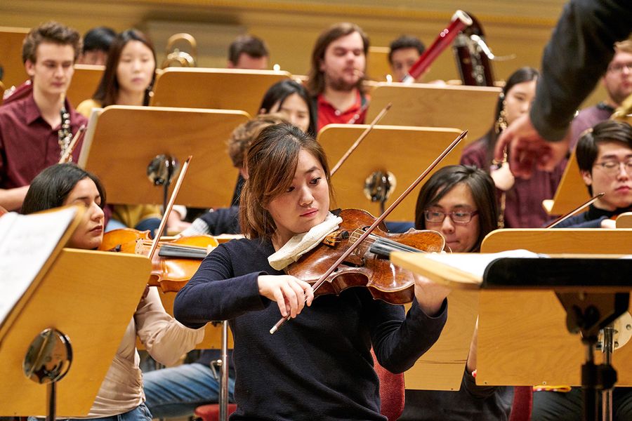 Studentin spielt Bratsche inmitten von Studierenden mit Instrumenten während einer Probe