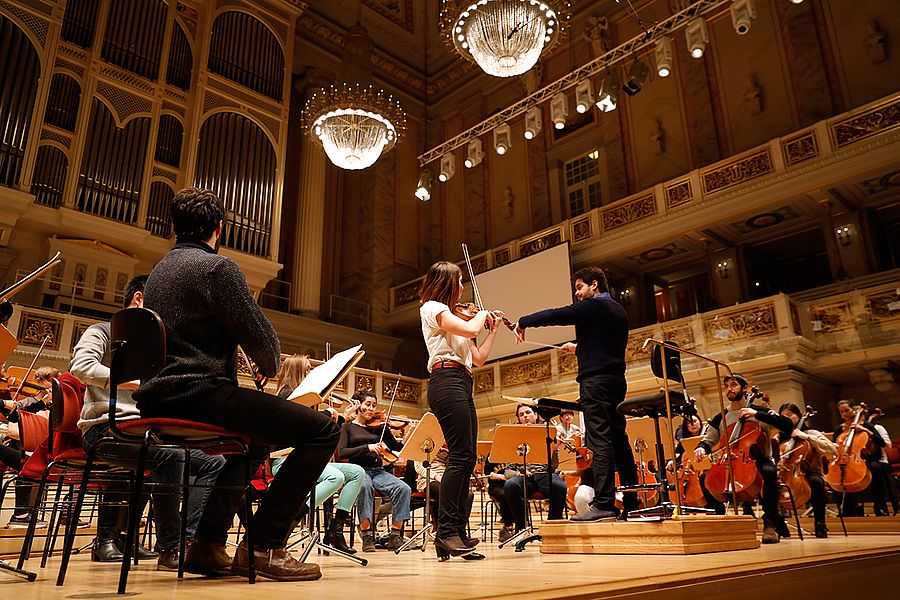 Geigensolistin und Dirigent vor einem Orchester aus Studierenden