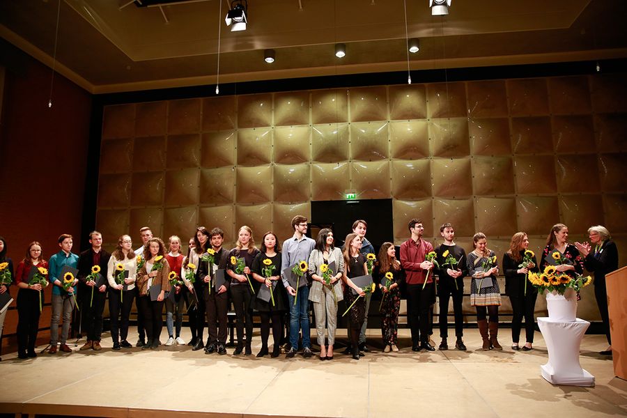 Stipendiaten mit Sonnenblumen und Urkunden auf einer Bühne