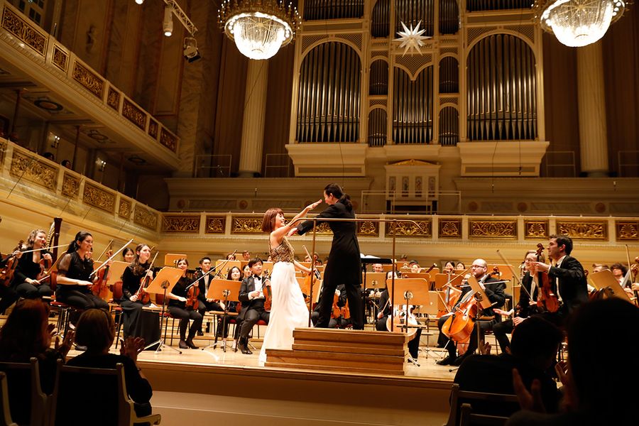 Geigensolistin und Dirigentin umarmen sich auf der Bühne vor dem Orchester