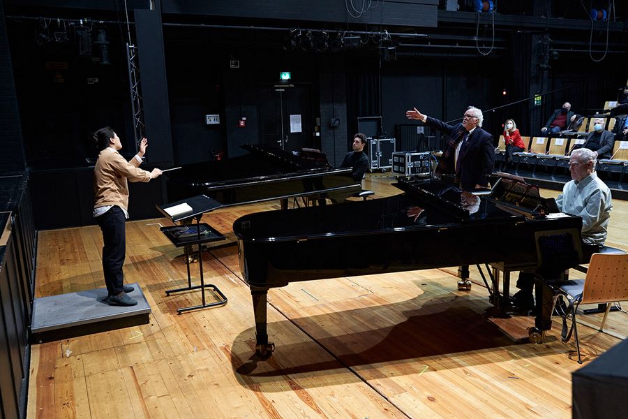 Dirigierende Studentin mit zwei Pianisten an Flügeln auf einer Bühne mit Sir Donald Runnicles