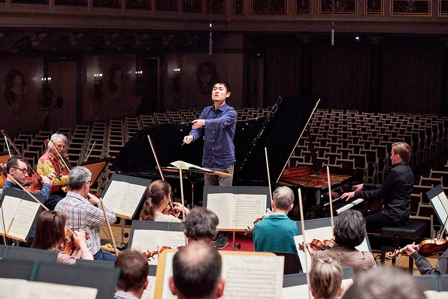 Student dirigiert ein Orchester in einem leeren Konzertsaal
