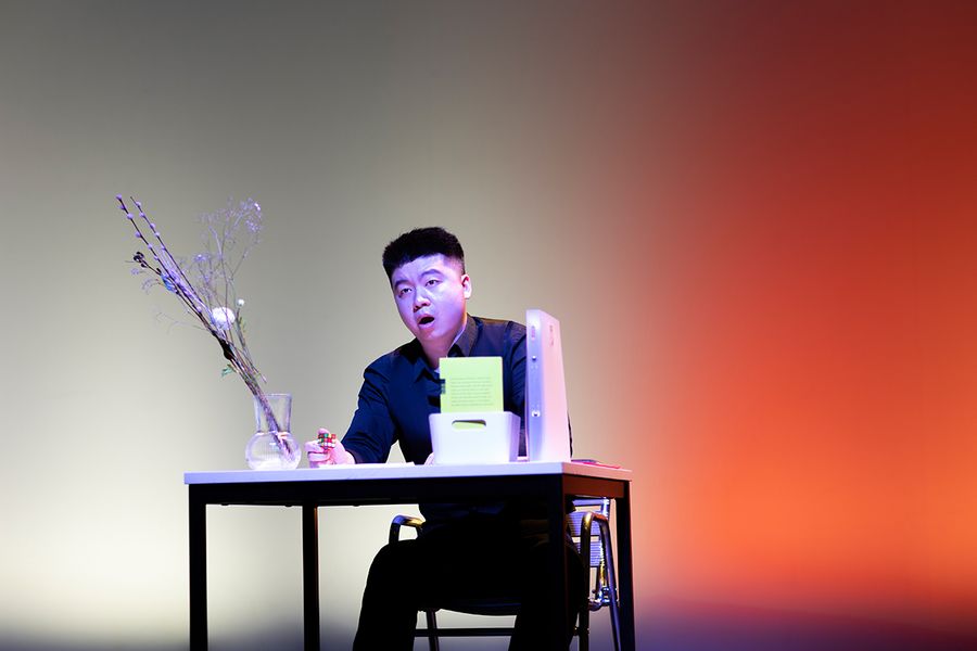 Gesangstudent sitzt an einem Tisch auf der bunt beleuchteten Bühne des Studiosaals
