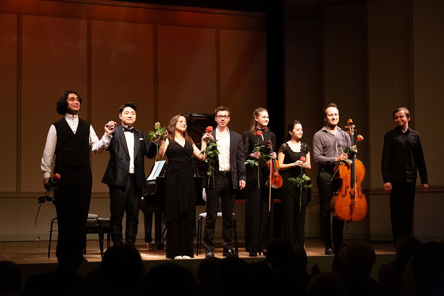 Personen mit Instrumenten und Rosen stehen in einer Reihe auf einer Bühne