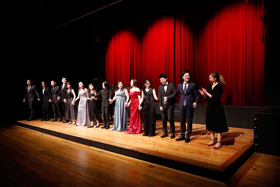 Gesangstudierende stehen in einer Reihe zum Applaus auf der Bühne des Studiosaals vor rotem Vorhang