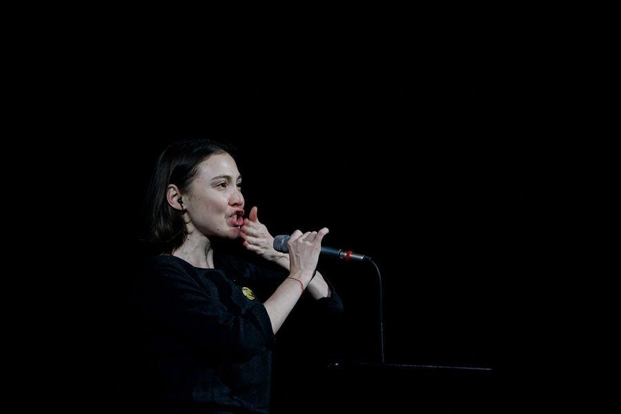 Eine Musikerin hält ein Mikrofon in der Hand und schlägt sich mit der Hand auf den Mund