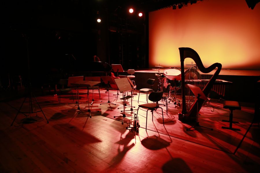 Bühne mit Stühlen, Notenstöndern, Schlagwerk und einer Harfe in buntem Licht