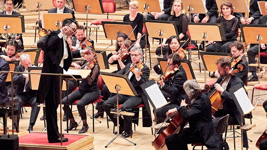 Harfensolist, Dirigent und Orchester auf einer Bühne während eines Konzertes