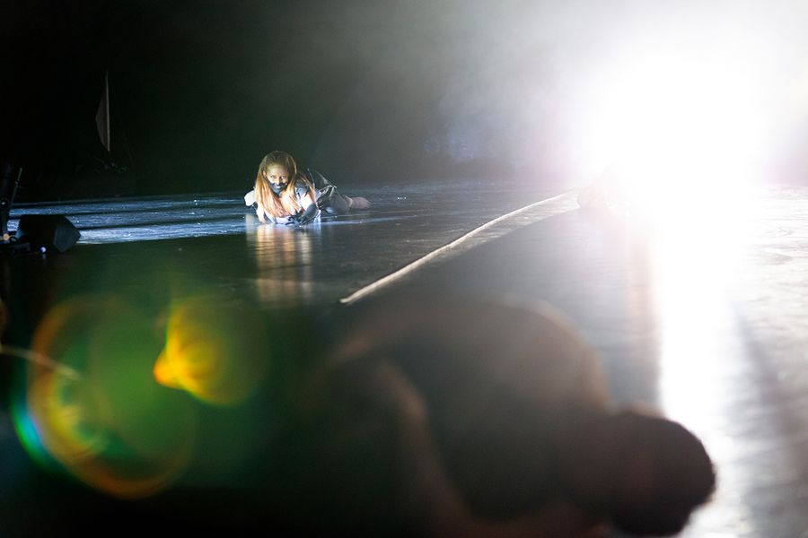 Studentin in Kostüm liegt bäuchlings auf einer Bühne im Scheinwerferlicht