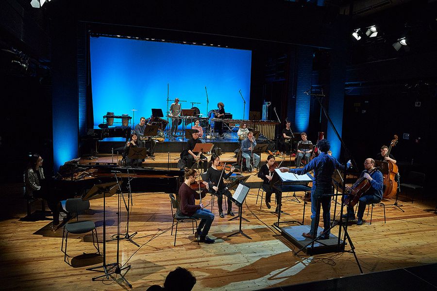 Hochschulprofessor dirigiert Studierenden-Ensemble auf einer blau ausgeleuchteten Bühne