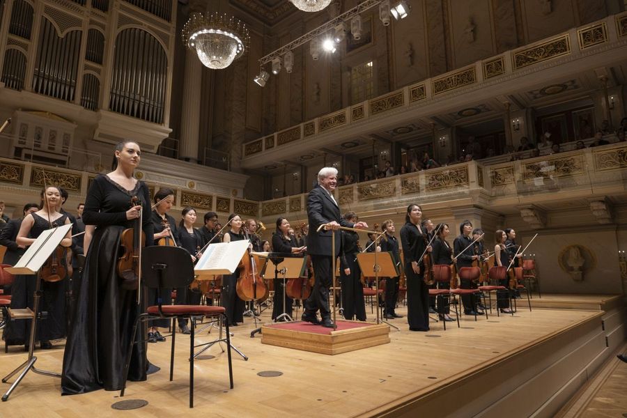 Solistin mit Geige und Dirigent am Dirigierpult stehen zum Applaus vor dem stehenden Orchester