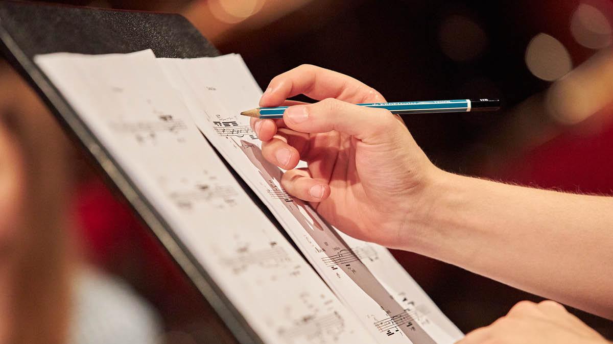 Eine Hand schreibt etwas mit Bleistift auf ein Notenblatt