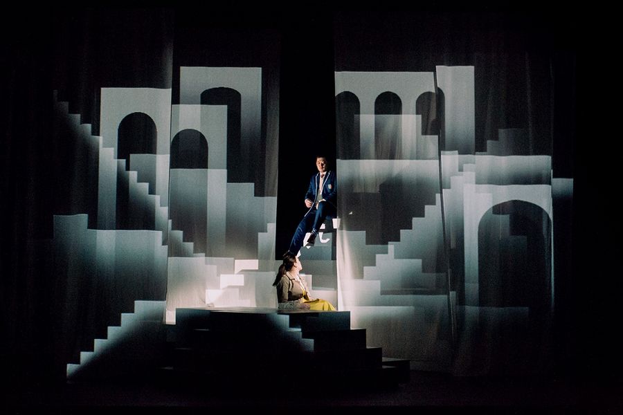 Zwei Gesangstudierende inmitten eines Bühnenbilds mit zahlreichen Treppen und Torbögen