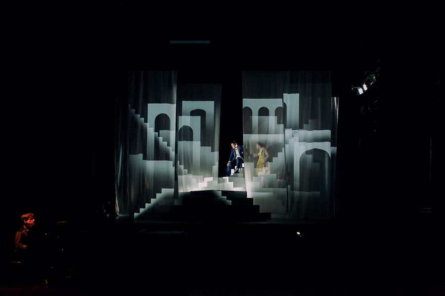 Zwei Gesangstudierende inmitten eines Bühnenbilds mit zahlreichen Treppen und Torbögen