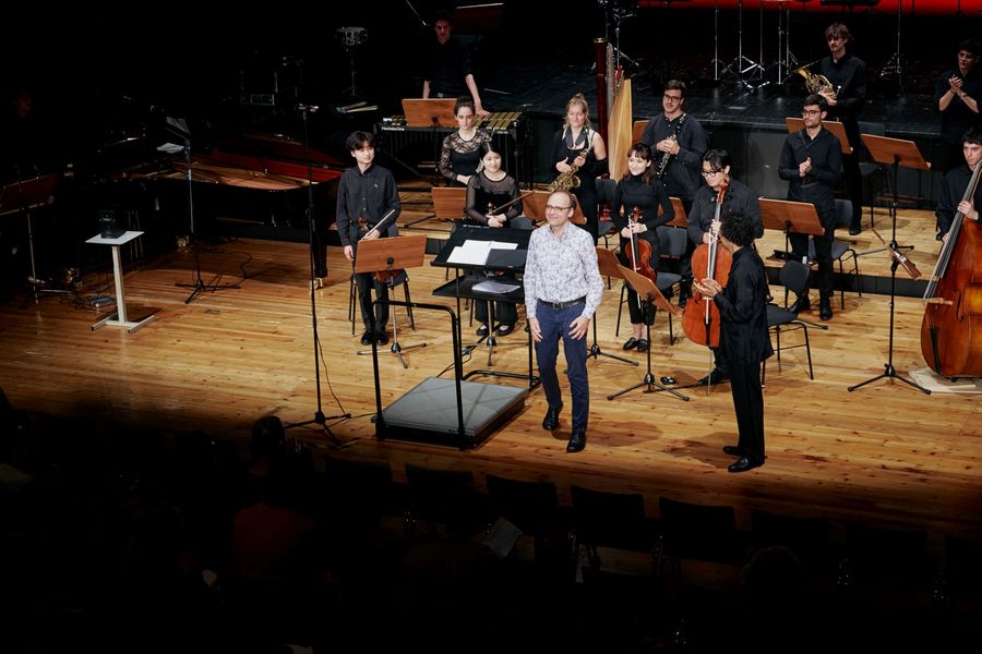 Ensemble, Dirigent und Mann in weißem Hemd nehmen Applaus auf der Bühne in Empfang