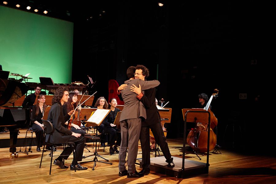 Pianist und Dirigent umarmen sich vor dem Ensemble auf einer Bühne