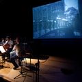 Orchester auf einer Bühne vor einem Bildschirm mit blauem Film