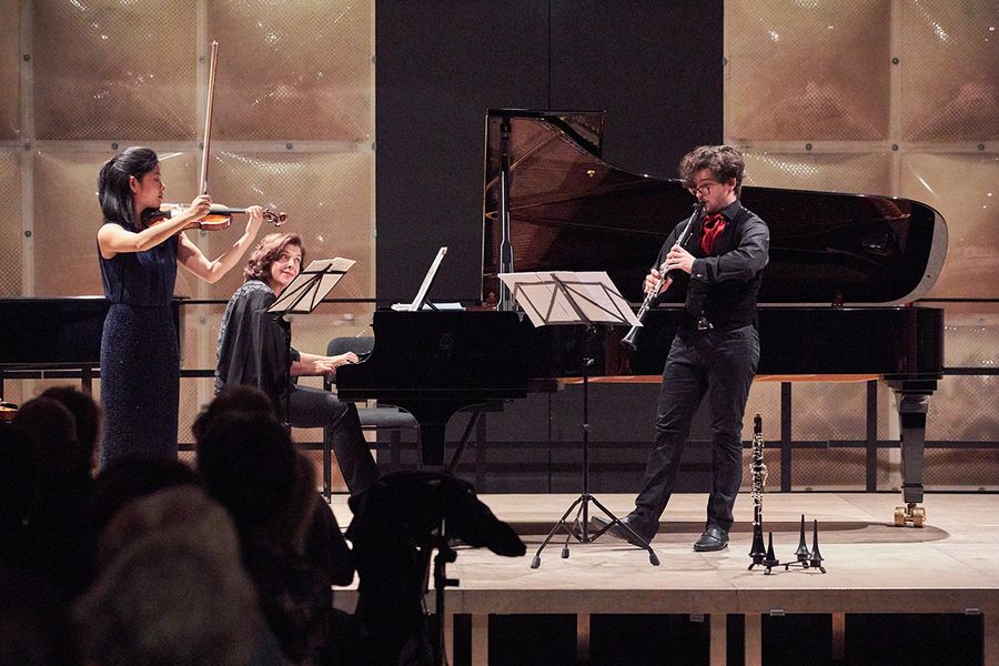 Studentin mit Geige, Student mit Klarinette, Frau am Flügel auf einer Bühne
