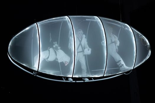 Drei als Astrinauten kostümierte Studierende in einer Art beleuchteten Raumschiff 