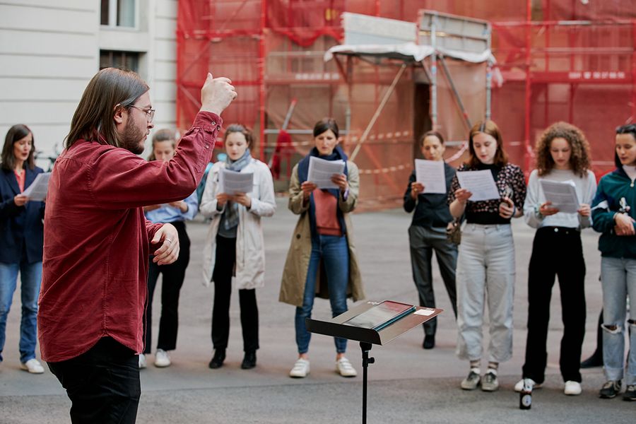 Student dirigiert und Hochschulangehörige stehen um ihn herum und singen